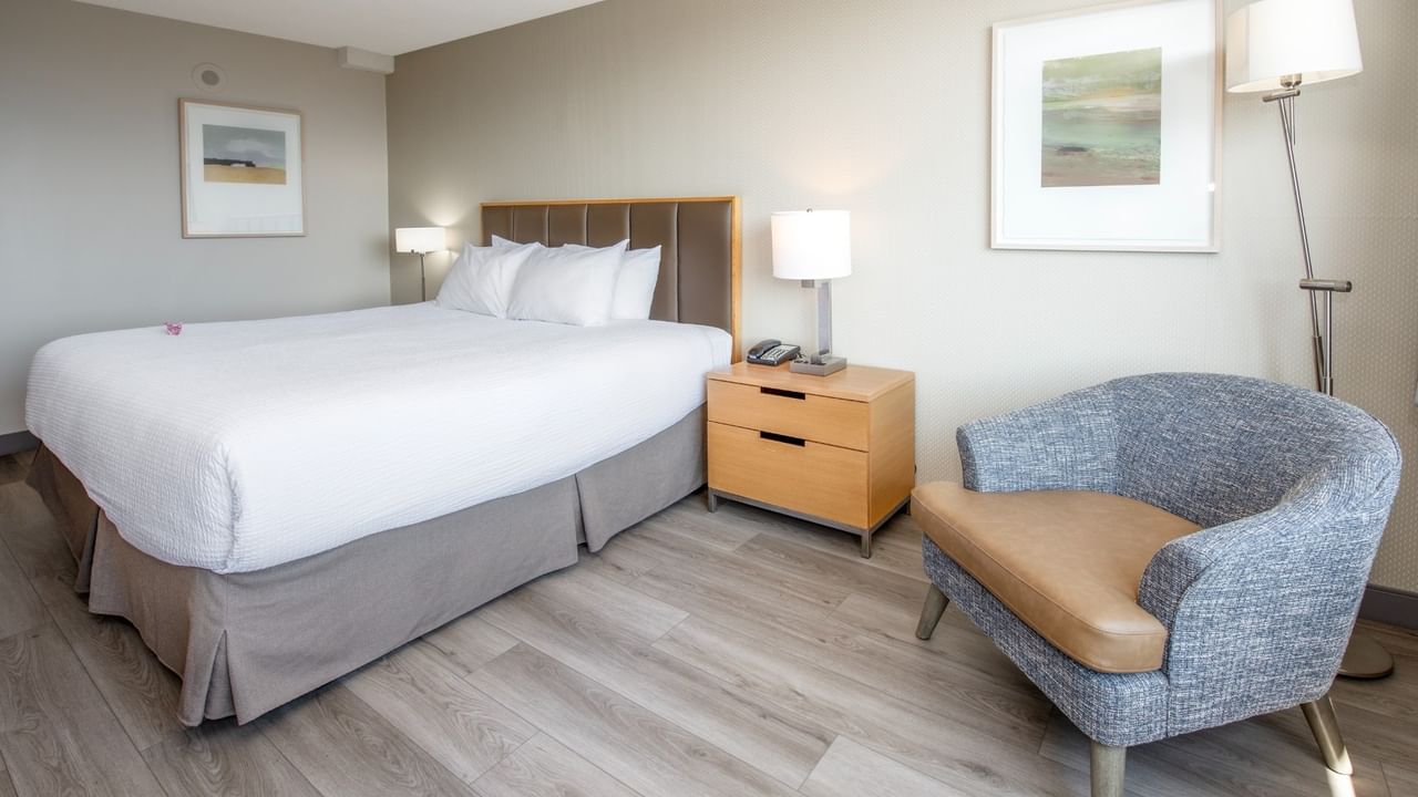 A hotel room with a king bed, nightstand, chair, and two framed pictures on the walls.