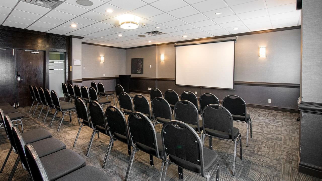 Meeting room with theater-style seating, projection screen, and modern lighting at Coast Calgary University Area Hotel by APA
