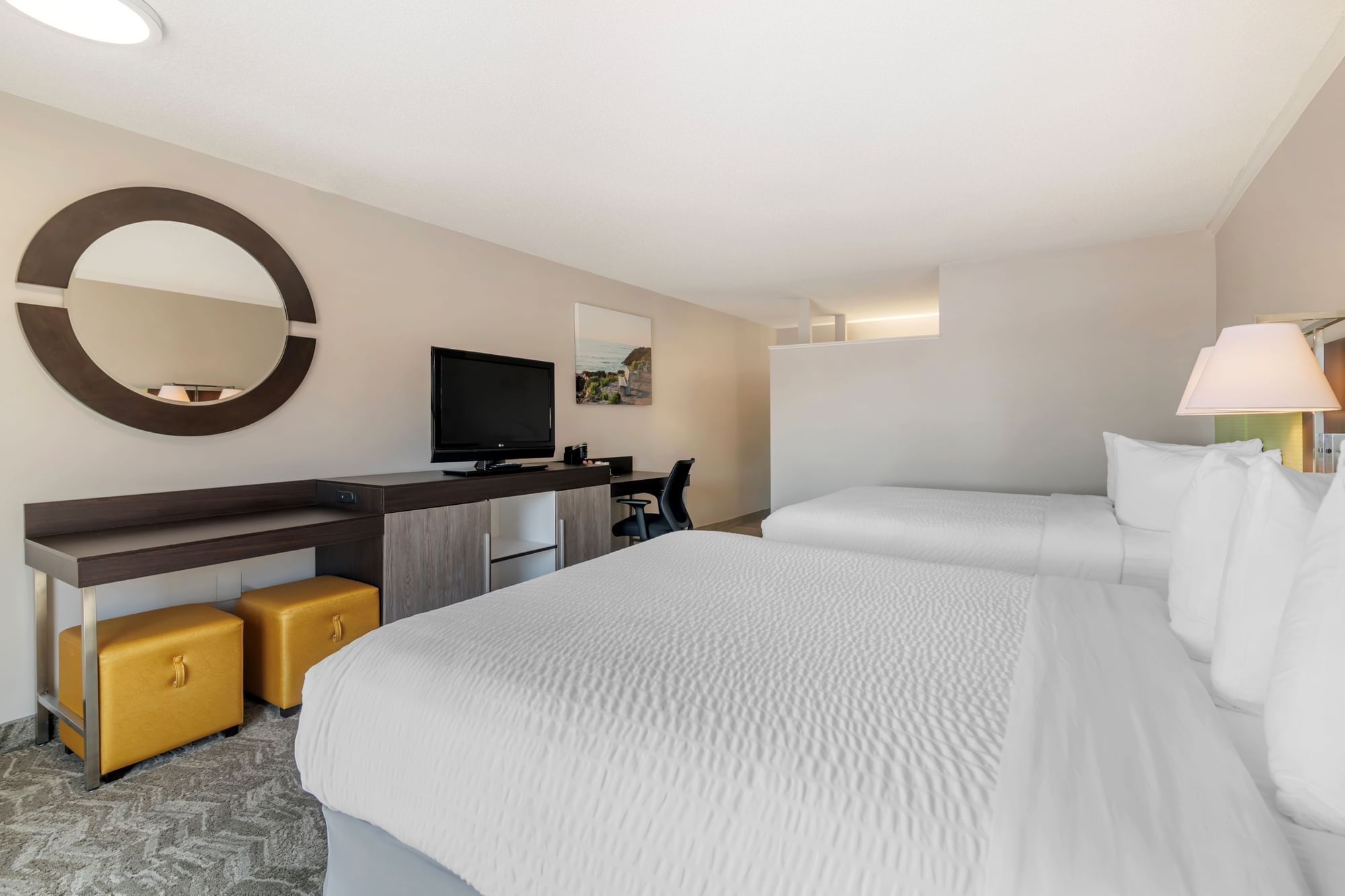 A hotel room with two queen beds, a desk with a TV, and a mirror on the wall.