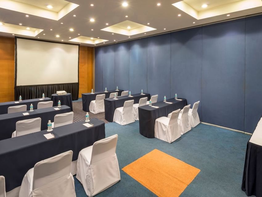 Classroom set-up with a projector screen and carpeted floors in the Berlin Venue at Real Inn San Luis Potosi