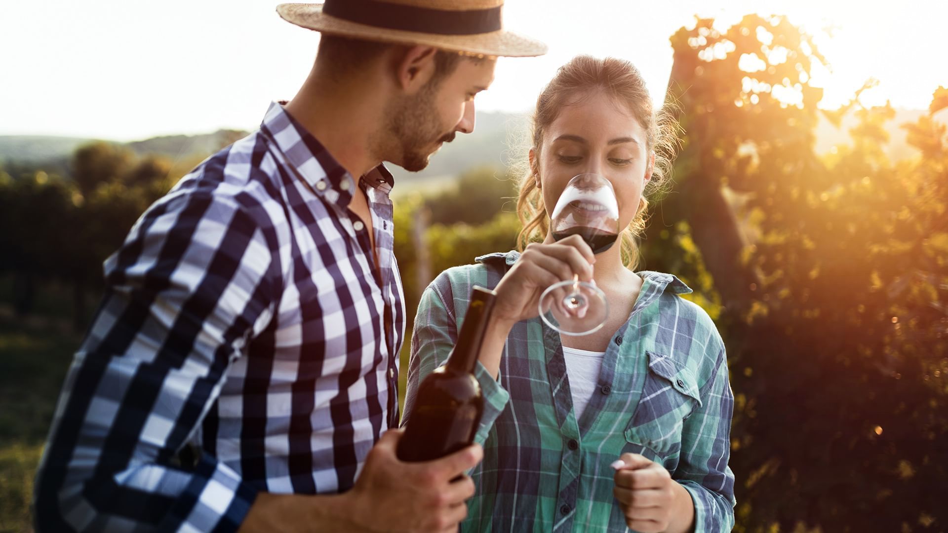 Couple enjoying wine in a vineyard at sunset, surrounded by lush greenery near Coast Penticton Hotel