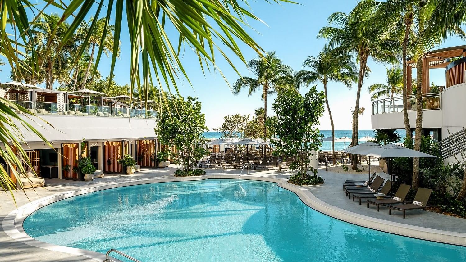 Tropical lagoon pool deck with resort loungers, cabanas, and palm-lined pathways.