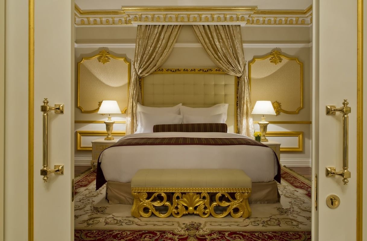 غرفة نوم فاخرة بديكورات ذهبية وسرير مزدوج مع ستائر كلاسيكية ومرايا جدارية في Warwick Doha