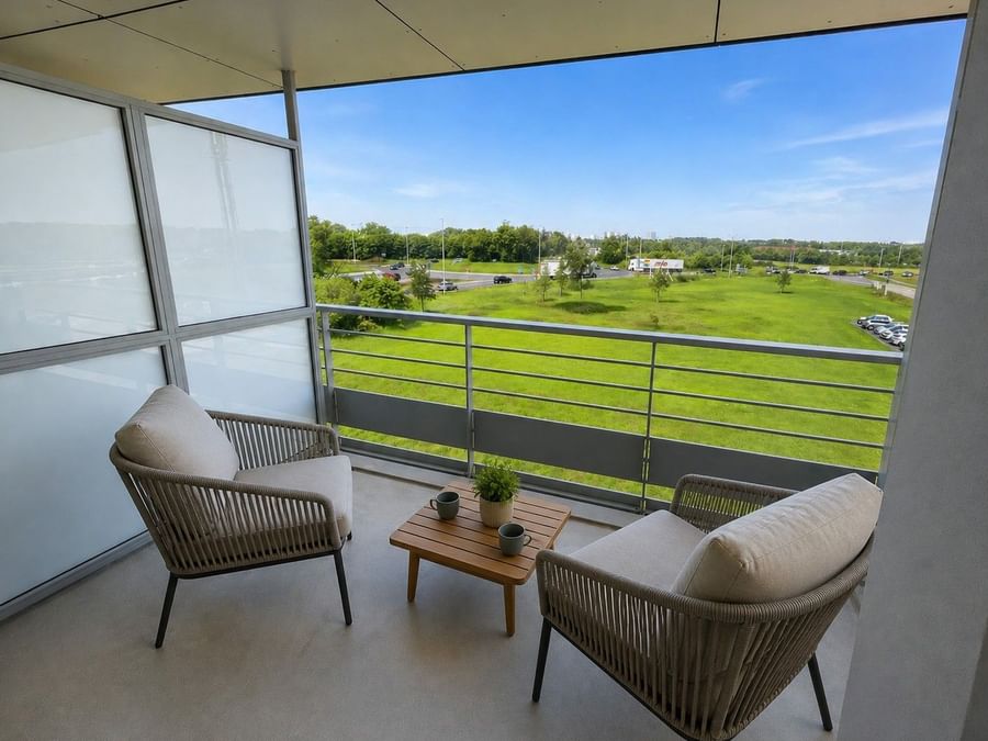 Deux fauteuils et table basse sur balcon vue sur pelouse à Osmo Hôtel Chantepie