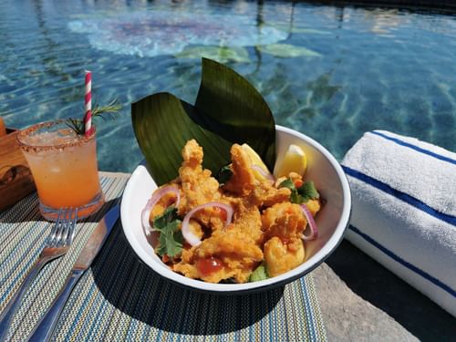 Fried fish & onions in a bowl, with a cocktail beside the pool at Sirenas Restaurant in Hacienda del Mar Los Cabos.