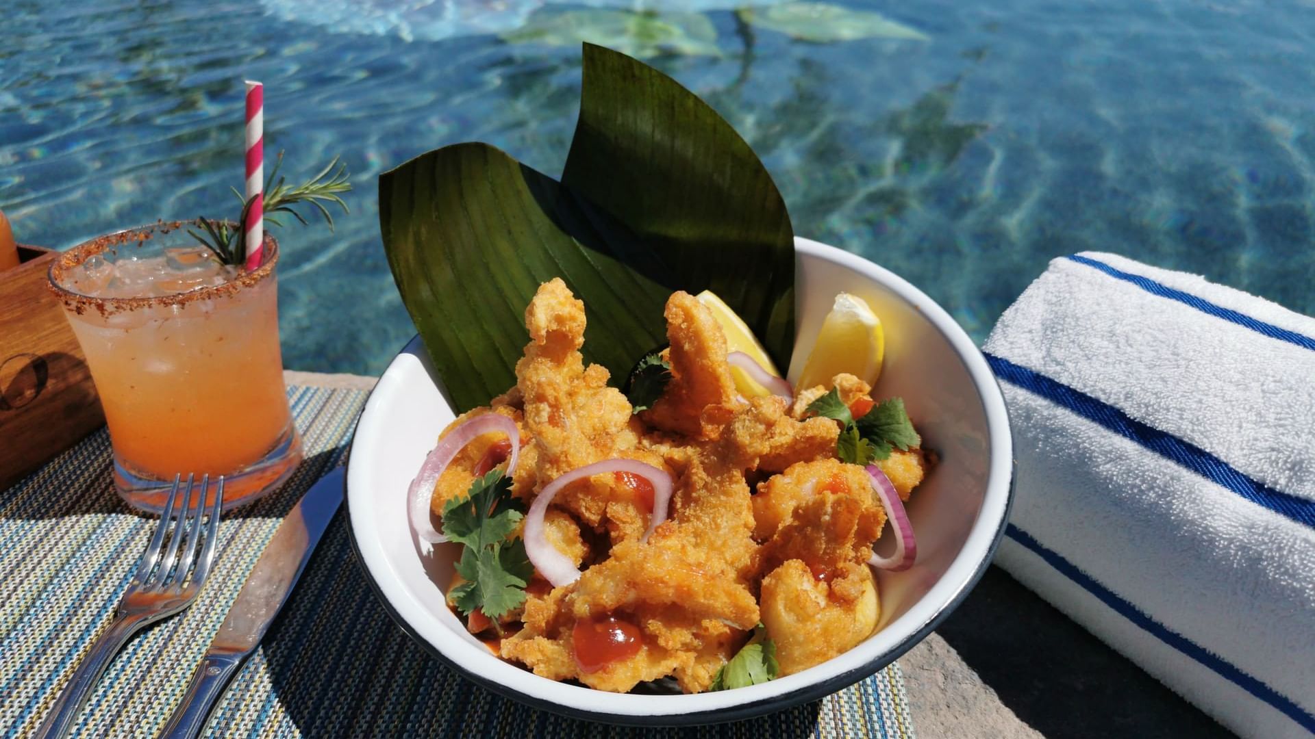 Fried fish & onions in a bowl, with a cocktail beside the pool at Sirenas Restaurant in Hacienda del Mar Los Cabos.
