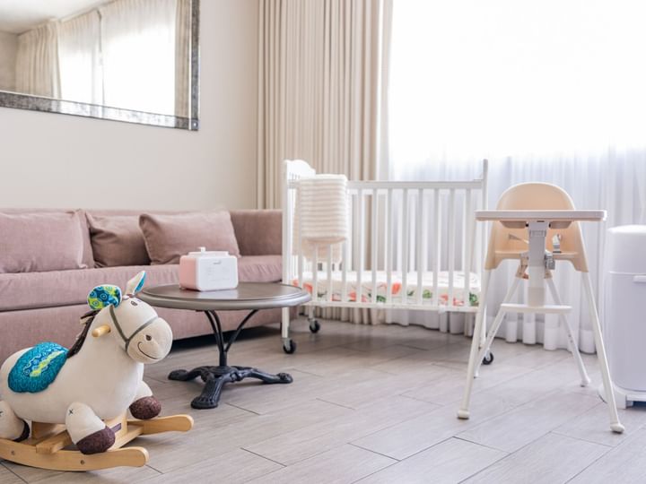 A furnished living room with a crib, high chair, and toys.