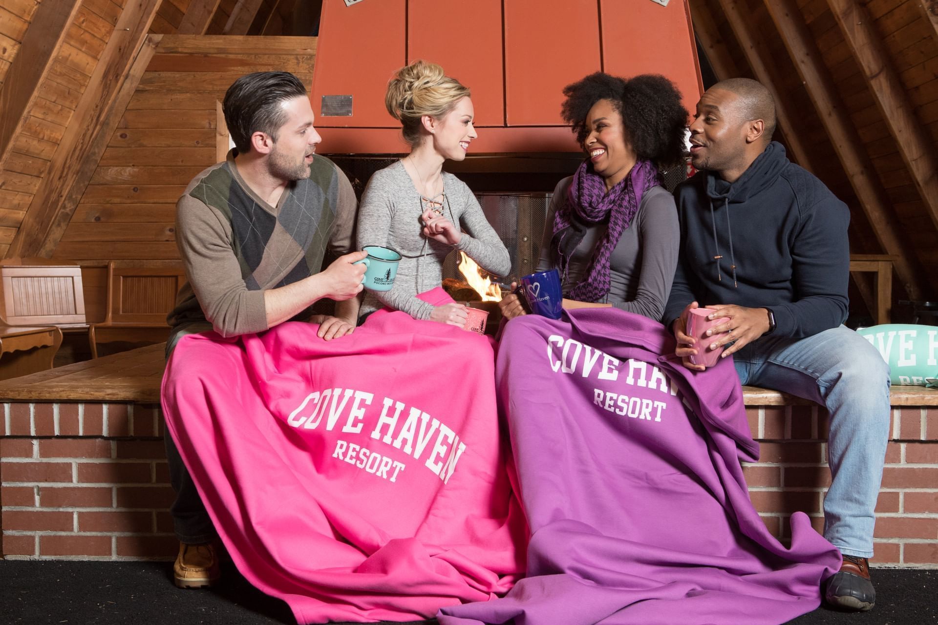 Four people relax together in a cozy cabin, wrapped in colorful blankets at Cove Pocono Resorts