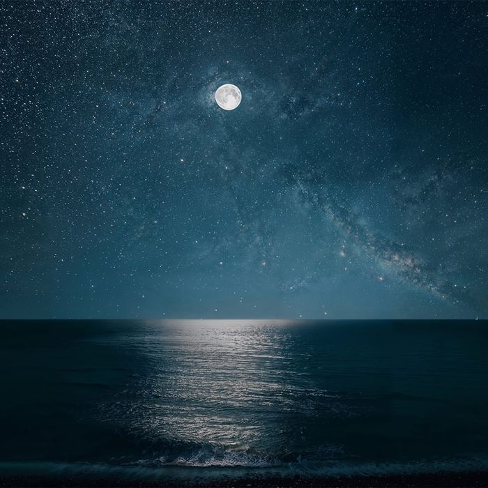 Nachtaufnahme des Meeres mit Vollmond und Sternen, Mondlicht spiegelt sich auf Wasseroberfläche.