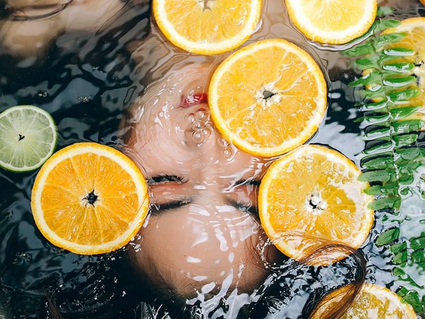 Image of a woman submerged in water with lemon slices floating in it