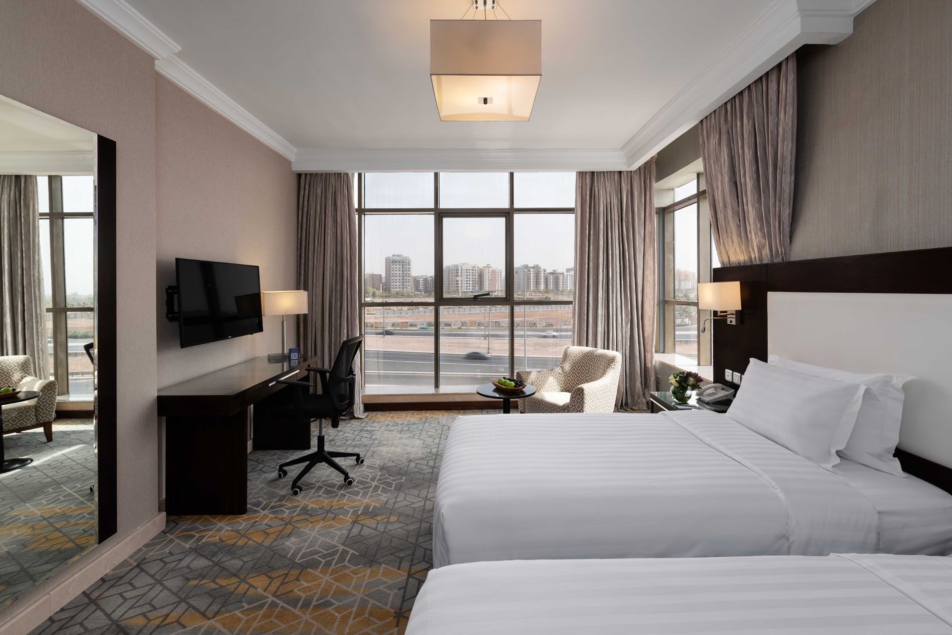 Wall-mounted TV, work desk, and cozy lounge chair by the beds in the Superior Room with city views at Warwick Hotel Jeddah