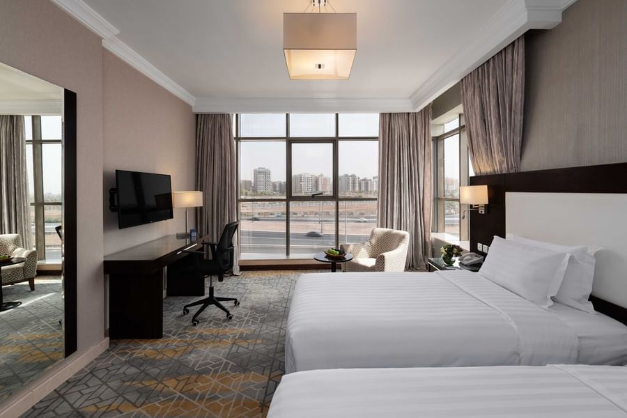 Wall-mounted TV, work desk, and cozy lounge chair by the beds in the Superior Room with city views at Warwick Hotel Jeddah
