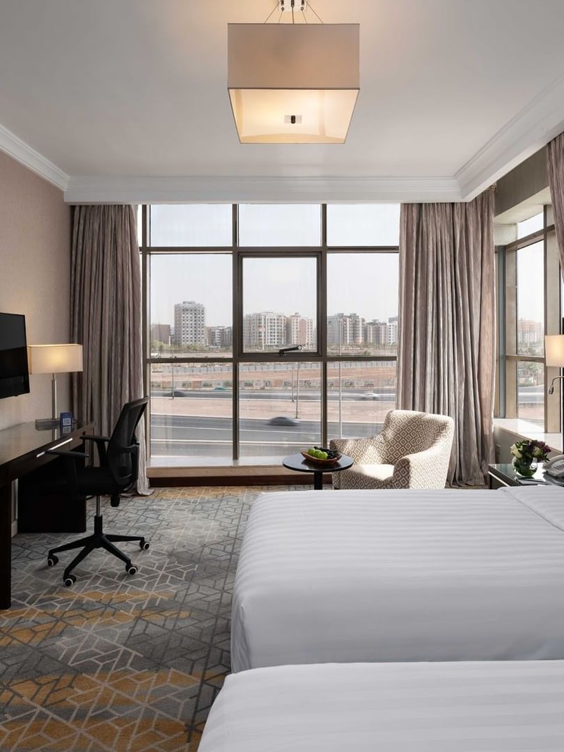 Wall-mounted TV, work desk, and cozy lounge chair by the beds in the Superior Room with city views at Warwick Hotel Jeddah