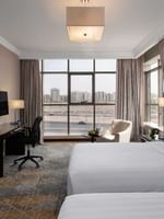 Wall-mounted TV, work desk, and cozy lounge chair by the beds in the Superior Room with city views at Warwick Hotel Jeddah