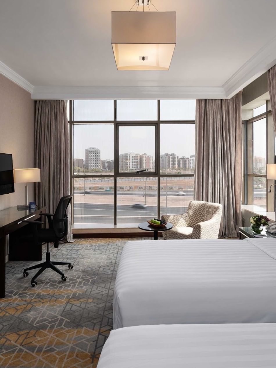 Wall-mounted TV, work desk, and cozy lounge chair by the beds in the Superior Room with city views at Warwick Hotel Jeddah
