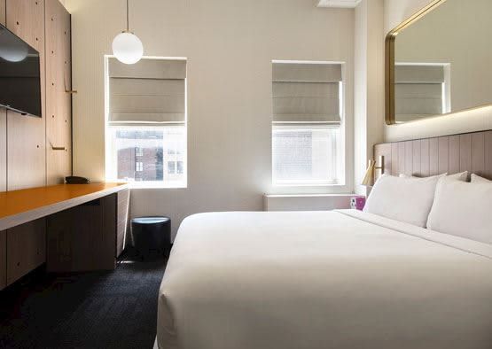 A hotel room with a king-sized bed, desk, and two windows.