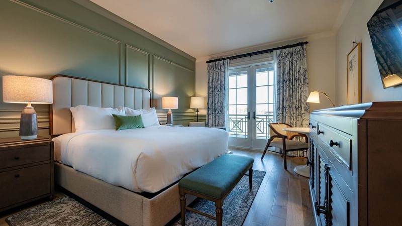 King bed with a cushioned headboard & wooden floors in Driving Range View King Room With Balcony at Camp Creek Inn