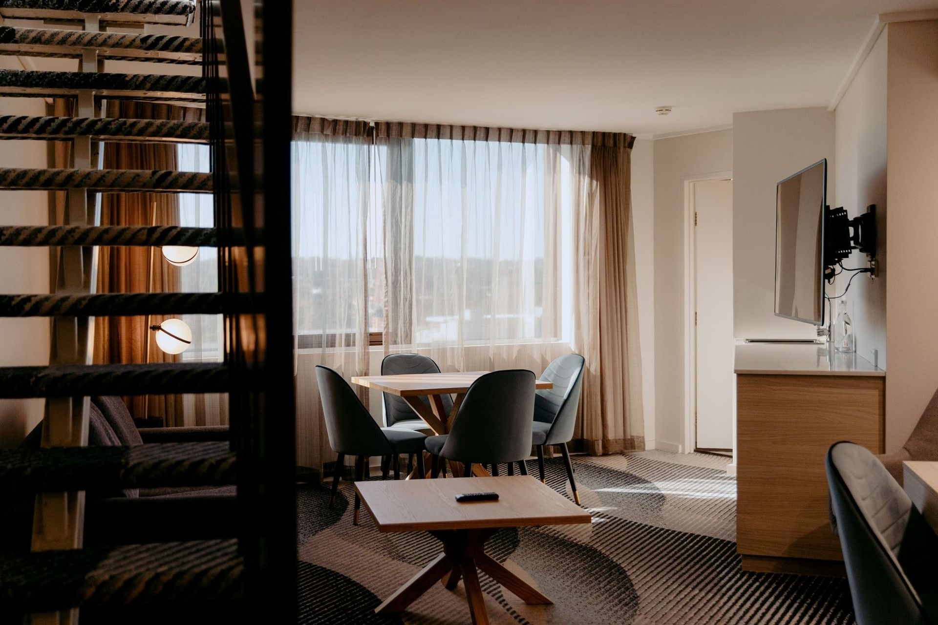Living room with table and chairs, TV, and a staircase at Novotel Sydney Parramatta