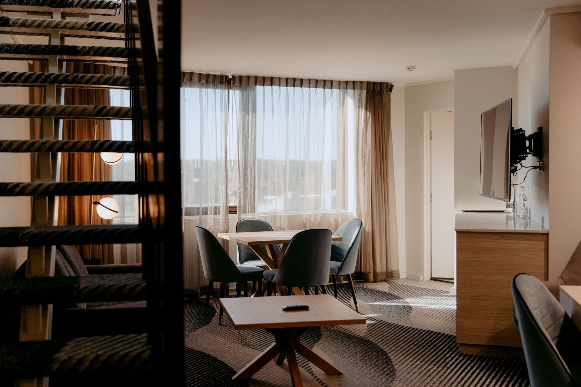 Living room with table and chairs, TV, and a staircase at Novotel Sydney Parramatta