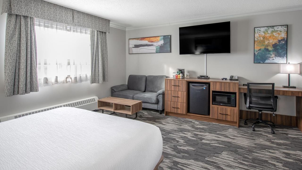 A hotel room with a bed, couch, desk, chair, television, and artwork.