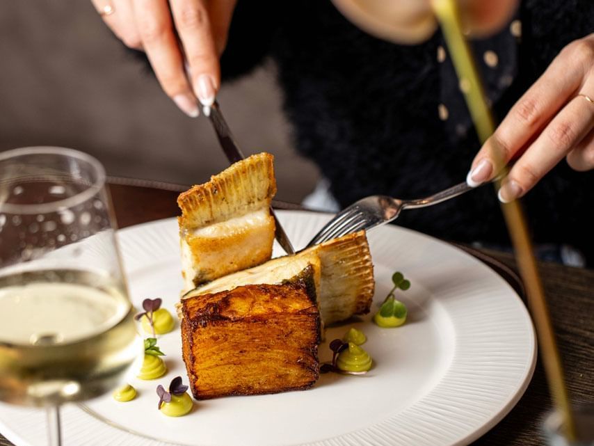 A woman enjoying a meal holding a fork and knife at EMME Restaurant