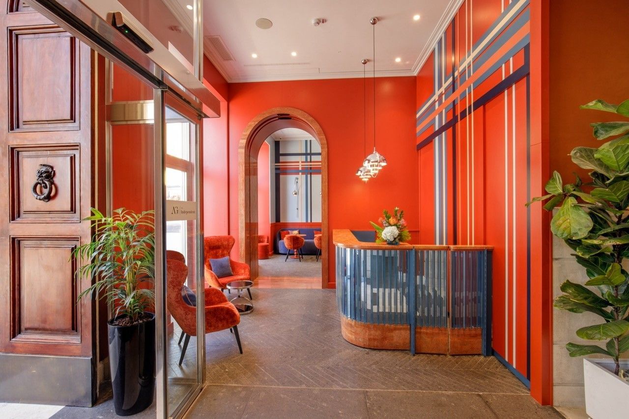 Lobby of the Independent Hotel in Rome with vibrant red-orange walls, modern striped wall design, stylish seating, a curved reception desk, and large plants creating a welcoming atmosphere.