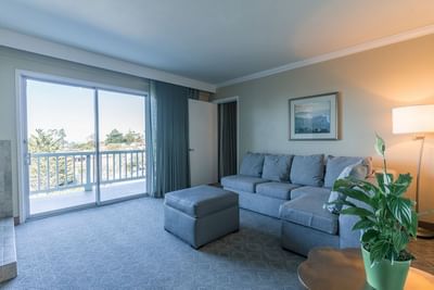 A cozy hotel living area with a large gray sectional sofa, ottoman, and sliding door to a balcony at Carmel Bay View Inn