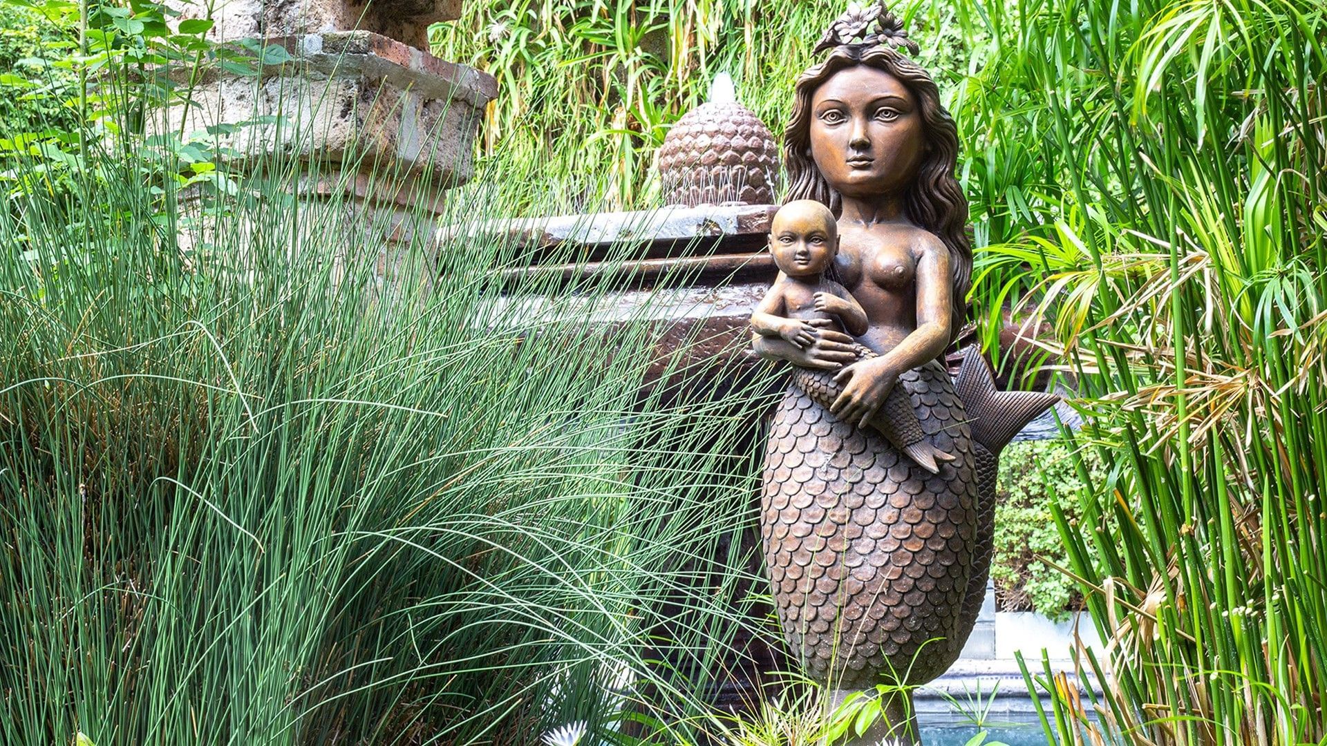 Intricate bronze mermaid statue holding a child near lush green garden plants at Quinta Real Guadalajara