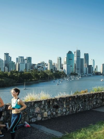 Runners on a pathway with a city skyline and river at Kangaroo Point near Sofitel Brisbane Central