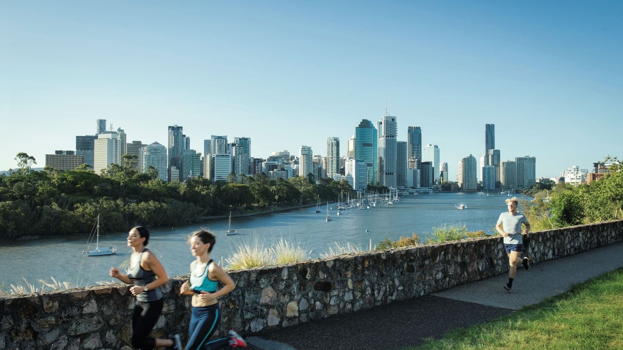 Runners on a pathway with a city skyline and river at Kangaroo Point near Sofitel Brisbane Central