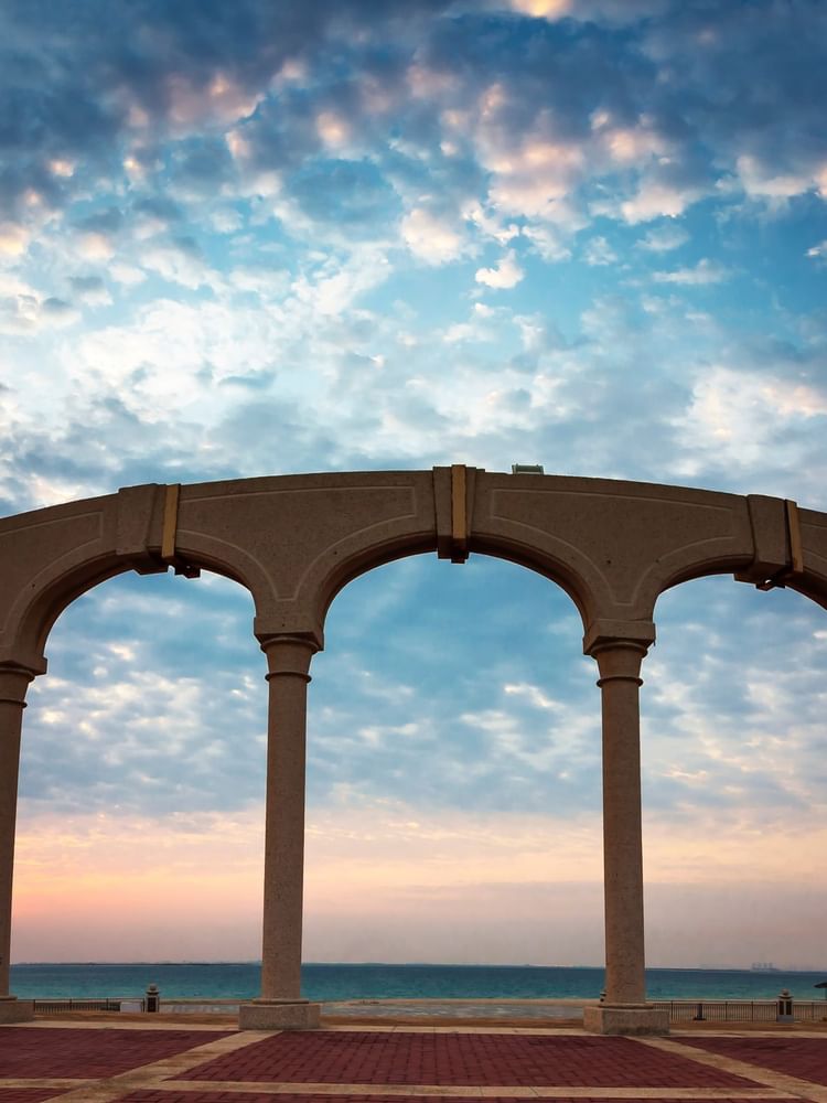 Tall stone arches in an open plaza, surrounding a view of the calm near Warwick Hotels & Resort