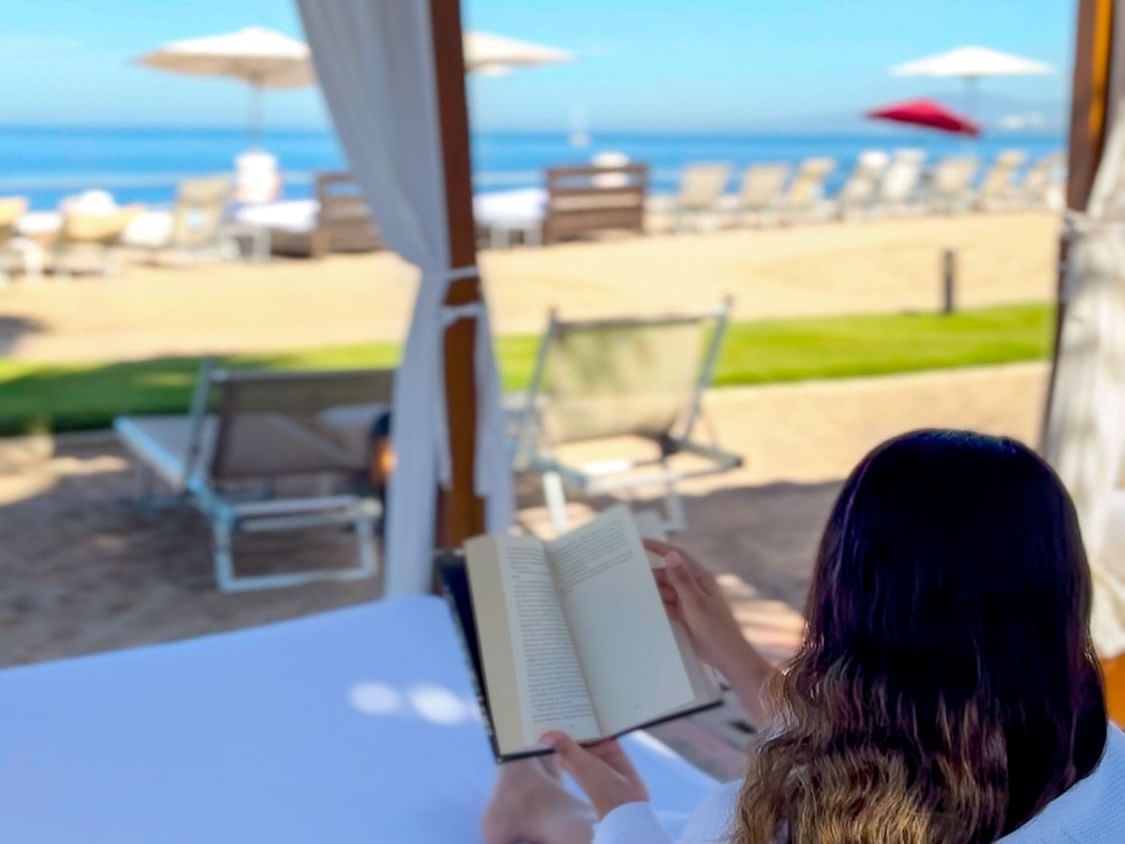 A woman reading a book on a bed at Plaza Pelicanos Grand Beach Resort
