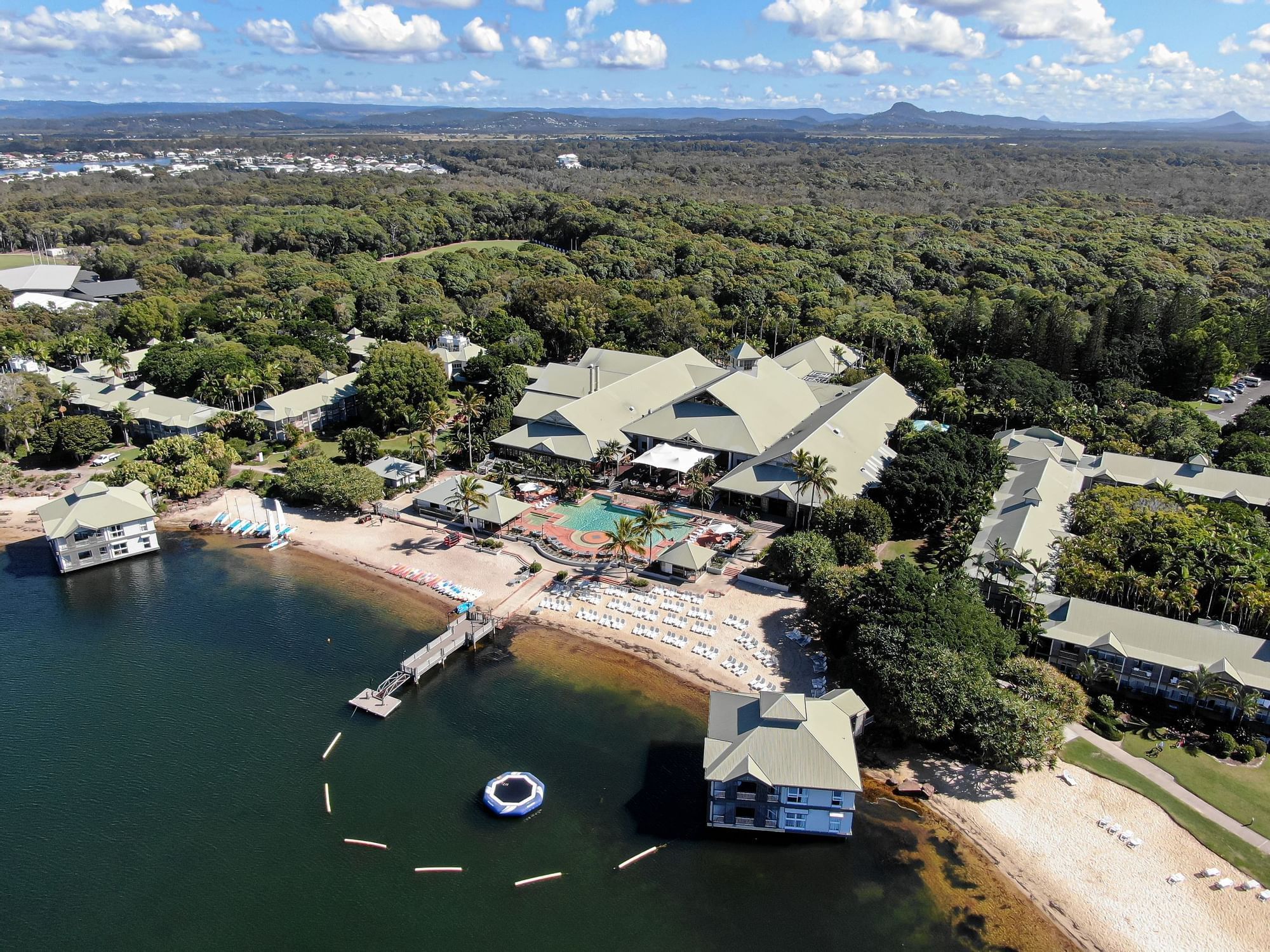 Aerial view of a Novotel Sunshine Coast Resort with sandy beach and lush greenery under a bright sky