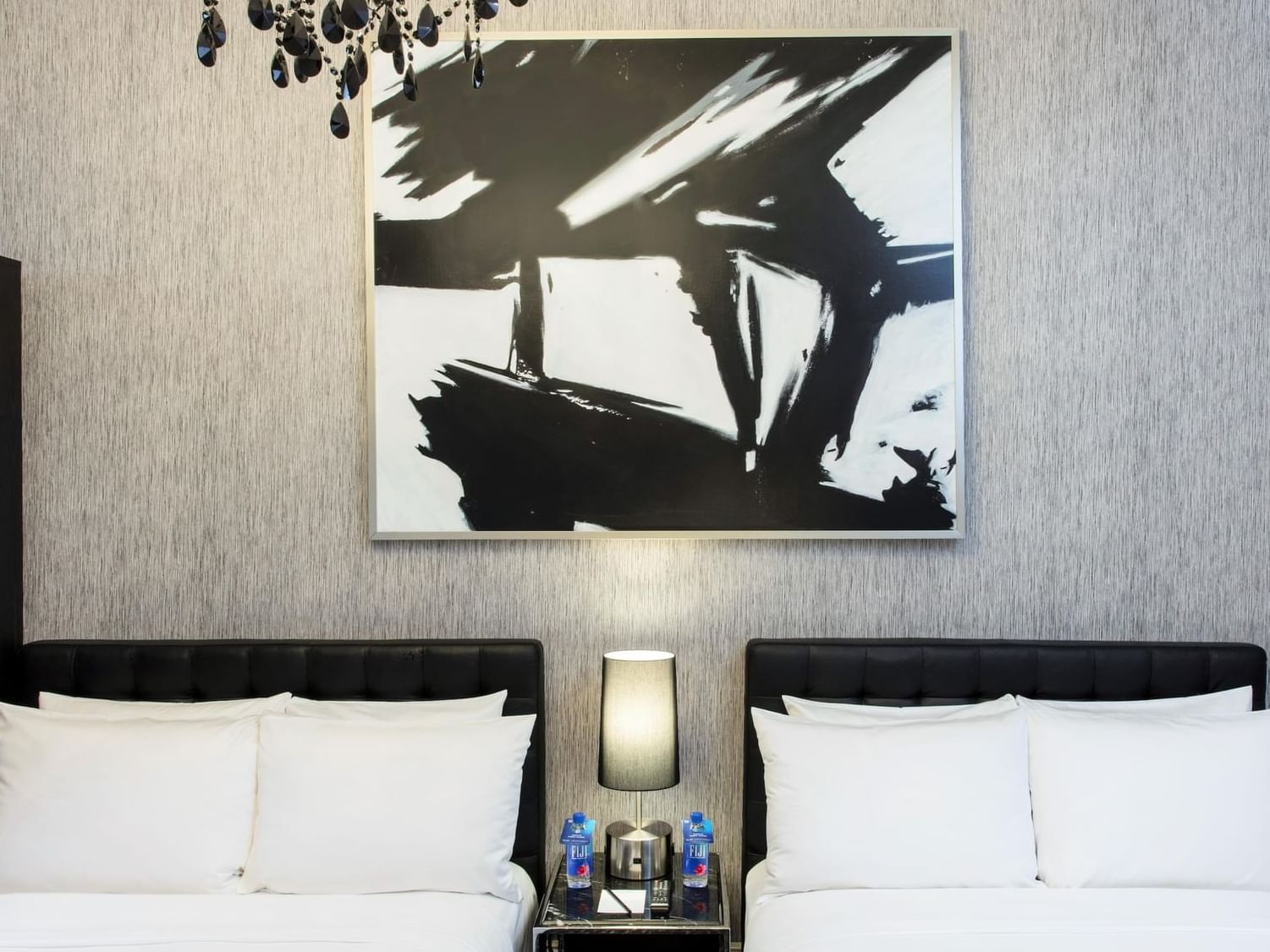 Two large white beds inside a hotel room with abstract art on the walls
