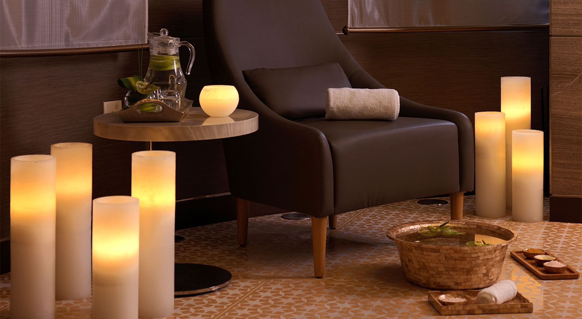 Spa Jardin setting with candles, a modern chair, table, pitcher of water, and wooden spa bowls at DAMAC Maison Cour Jardin