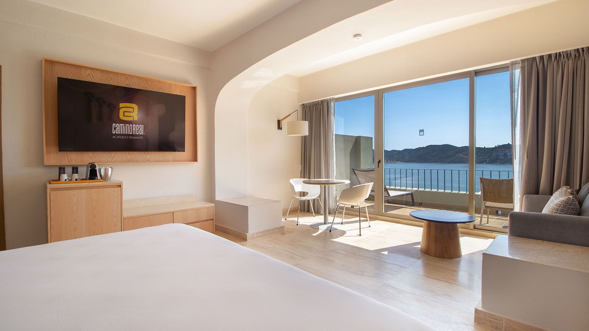Wall-mounted TV and sitting area by the bed in King Camino Real Club at Camino Real Acapulco Diamante
