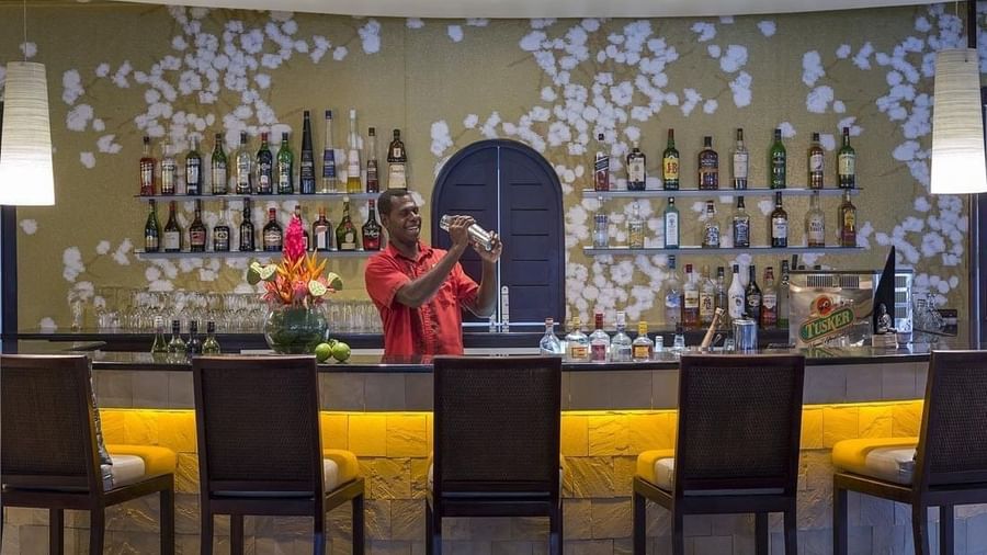 Bartender shakes cocktail behind Wild Ginger Restaurant & Bar with a floral-patterned wallpaper at warwick le lagon-vanuatu