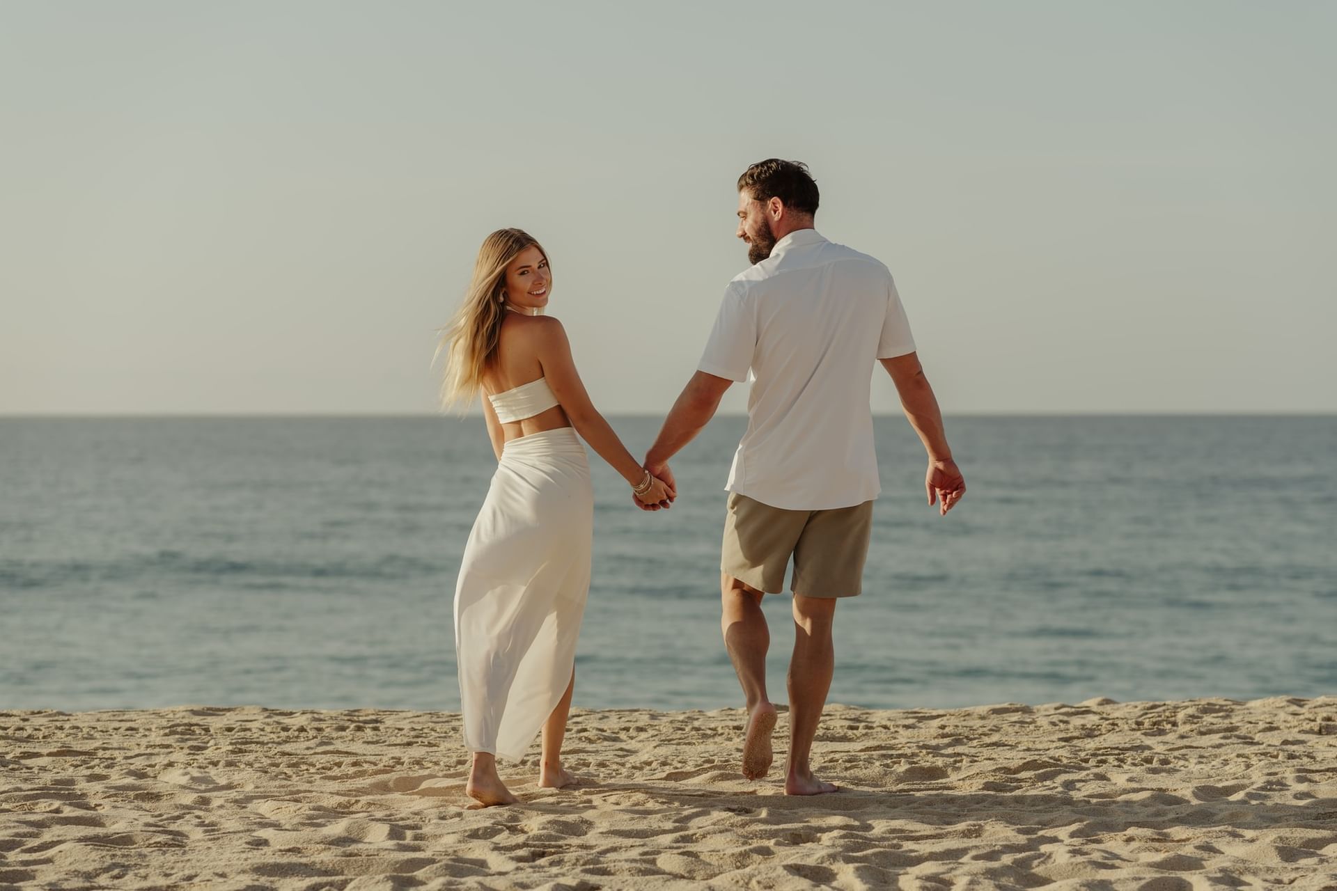 Pareja caminando de la mano por la playa del Hotel Marquis Los Cabos en México.