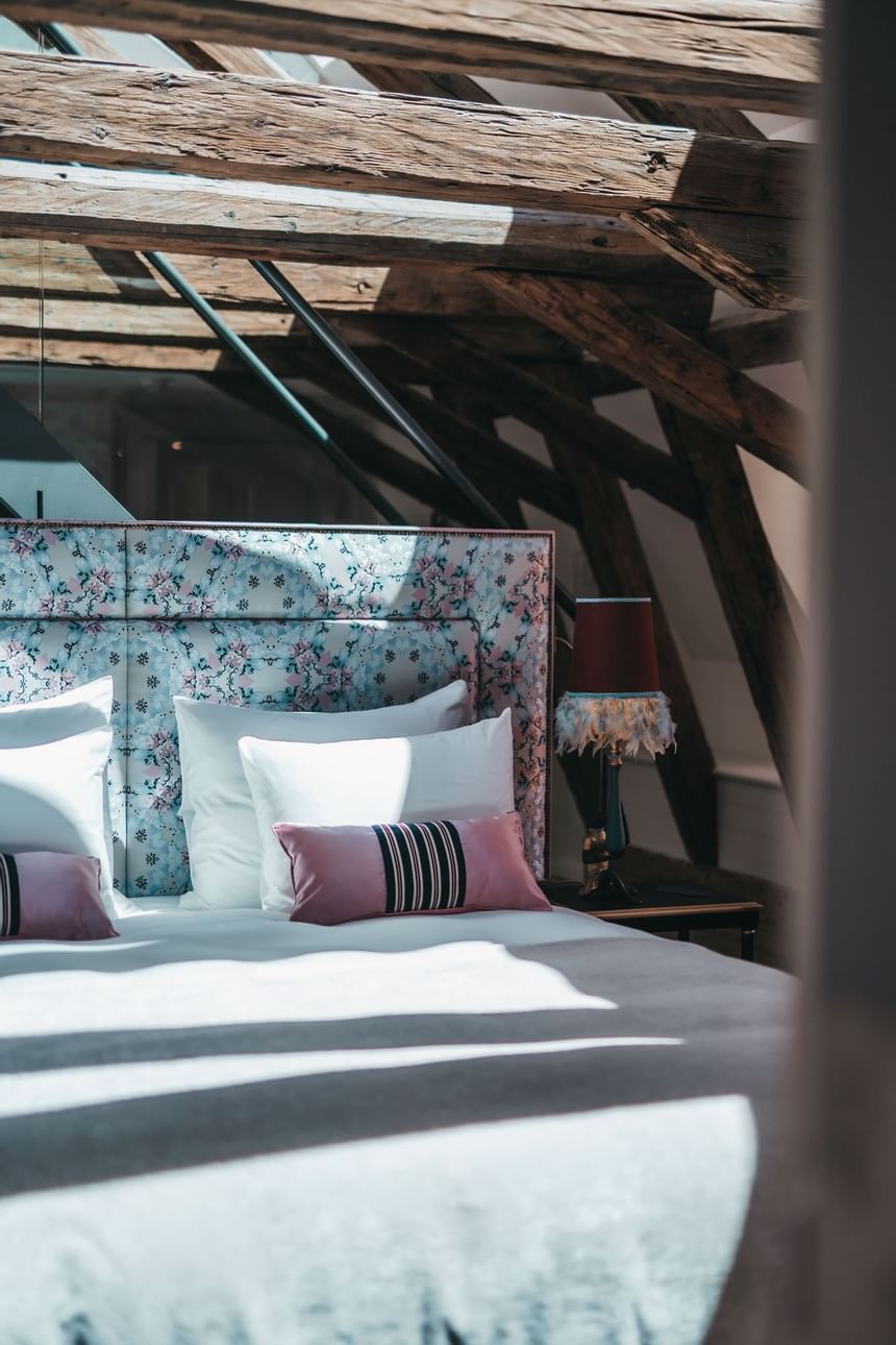 Ansicht eines Doppelbettes im THE LEO GRAND in Wien mit Fokus ein Bett mit darüberliegendem Dachgebälk im rustikalen Stil. 