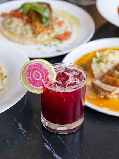 Cocktail garnished with a lime and radish slice served alongside dishes at The Ashbrook Hotel