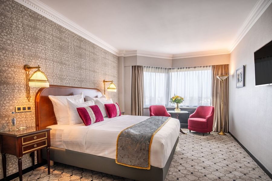 King bed between gold lamps and beside two red armchairs with vase on table in Deluxe Room at Hotel Barsey by Warwick