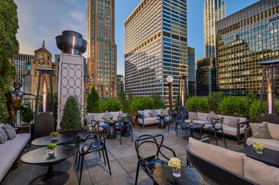 Outdoor lounge with sofas and black tables facing illuminated city skyscrapers at night at The Kimberly Hotel