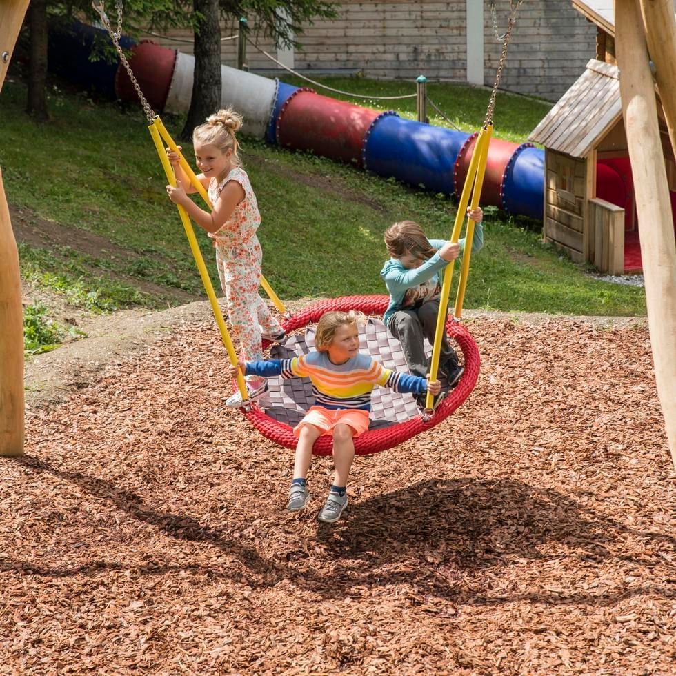 Kids playing on swing with wood chips on the ground at Katschhausen Kid's Adventure World near Falkensteiner Hotel Cristallo