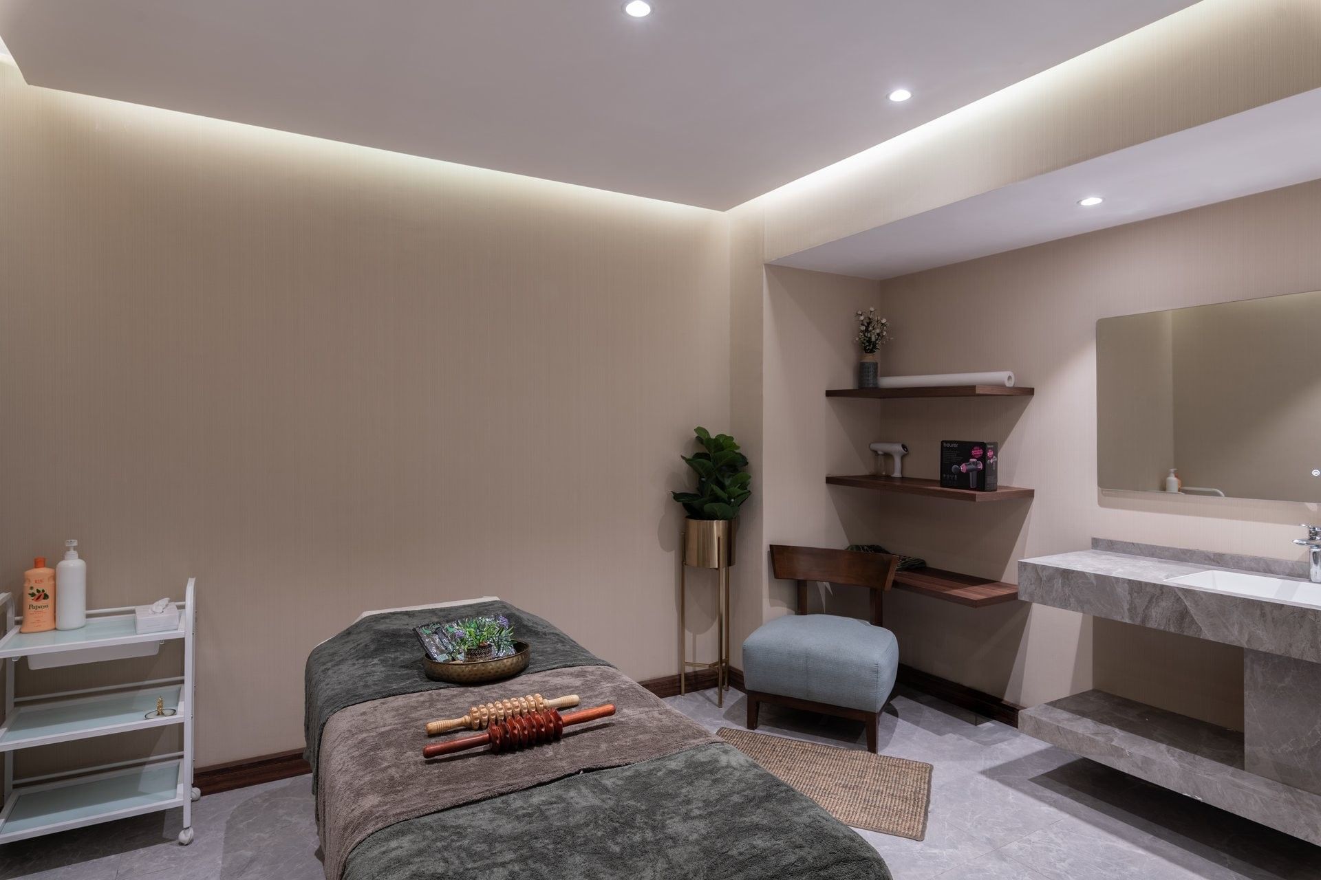 Massage table with rollers by a blue armchair and marble sink under soft lights in Golden Time Spa at Warwick Al Taif Hotel
