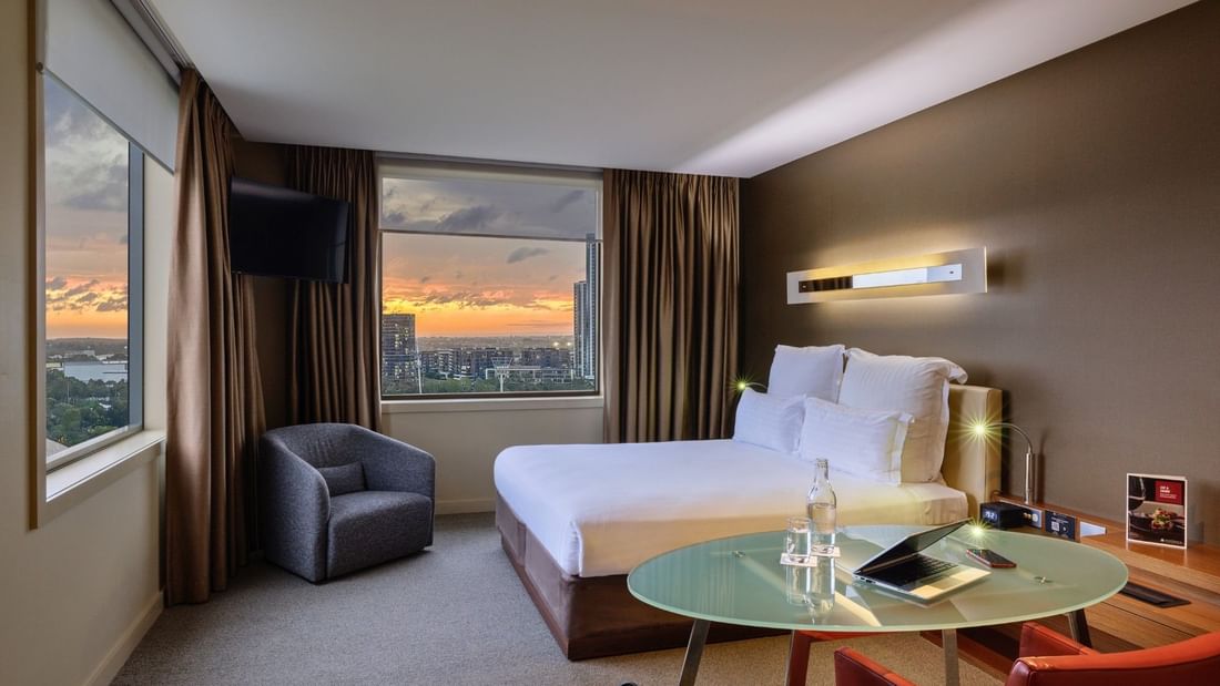 Modern hotel room with a bed, chair, and table at Pullman Sydney Olympic Park.