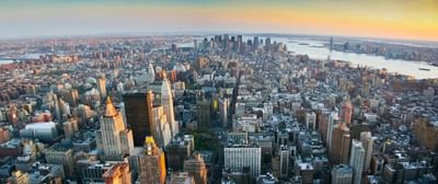Aerial view of a cityscape with numerous skyscrapers and a body of water at sunset.