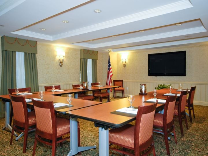 A meeting room with several tables and chairs, wine glasses, an American flag, and a TV screen on the wall.