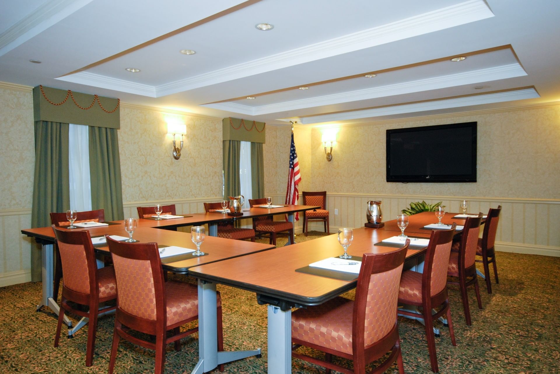 A meeting room with several tables and chairs, wine glasses, an American flag, and a TV screen on the wall.