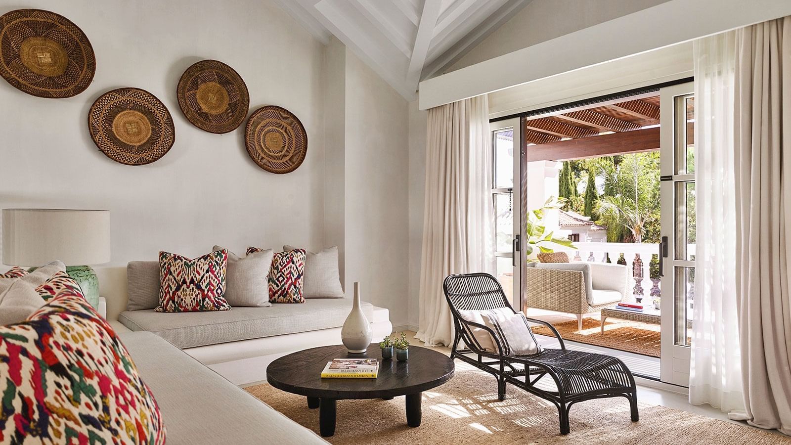 Four-Bedroom Villa living area with a built-in daybed, rattan chaise, wall art, & open sliding doors at Marbella Club