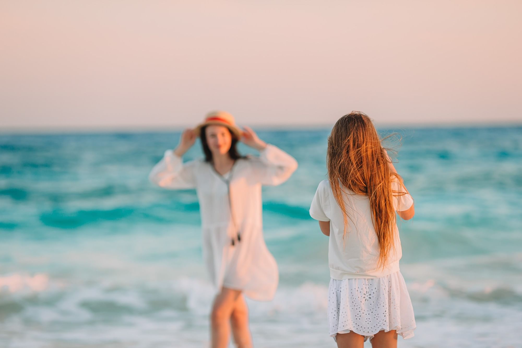 Two women standing on a beach with ocean waves in the background.